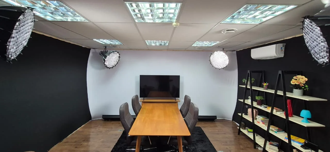 Sala clara de gravação com TV e mesa de reunião